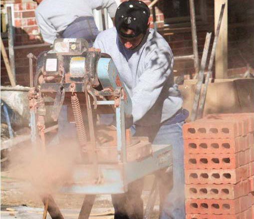 A construction worker cuts through a brick.