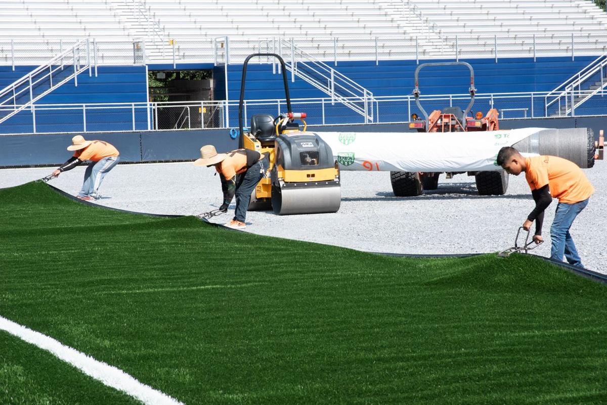 Workers install artificial turf at a high school stadium in Marietta, Ga.