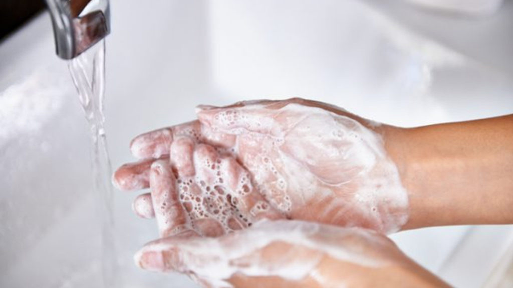 Water Shutoffs: Woman washing her hands at the kitchen sink. There are vegetables out of focus in the background.