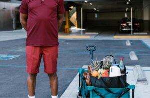 Man standing in a parking lot beside a cart filled with groceries