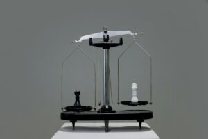 A balance scale with a black chess pawn on one side and a white chess king on the other.