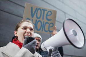 A protester shouting into a megaphone with a “Vote Choice” sign in the background.