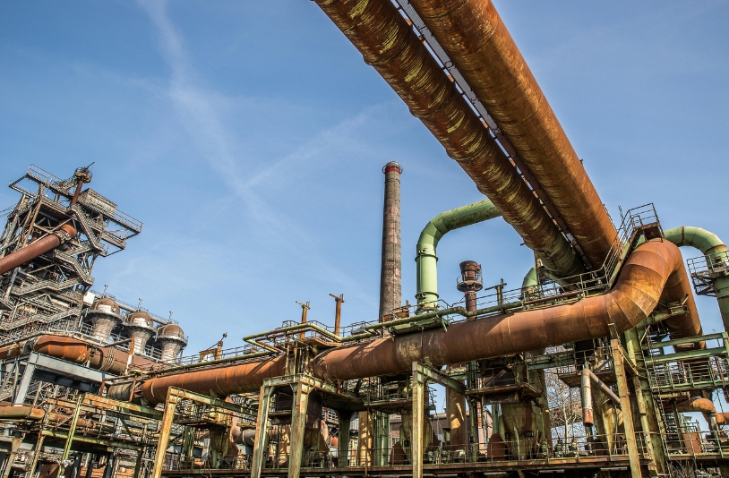 Rusty oil refinery pipes under blue sky.