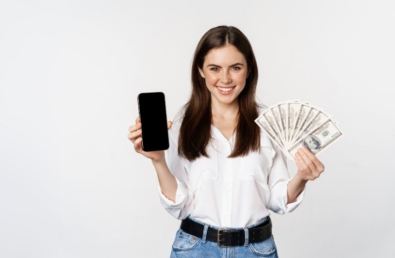 Woman showing mobile phone screen and cash money concept of microcredit and bank loans standing over