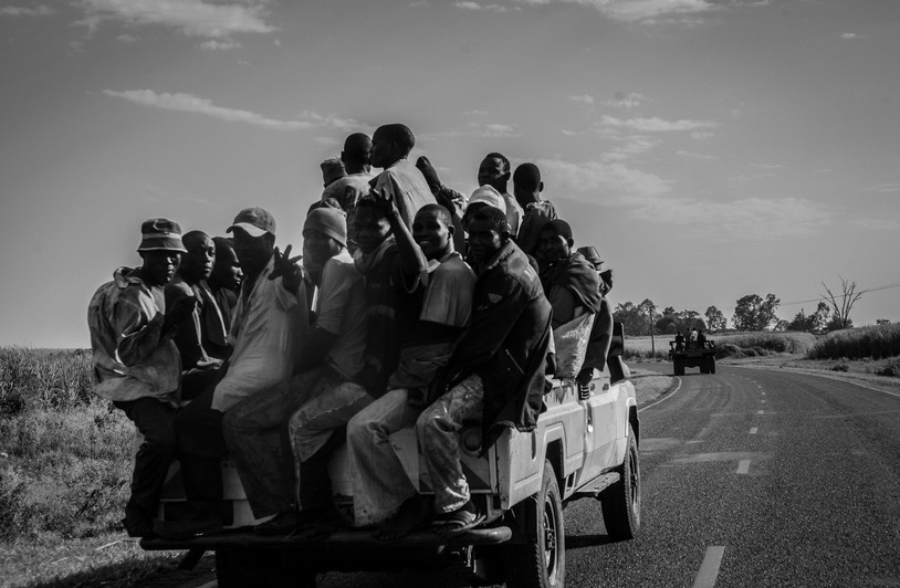 People sitting in the open bed of a pickup truck on a rural road