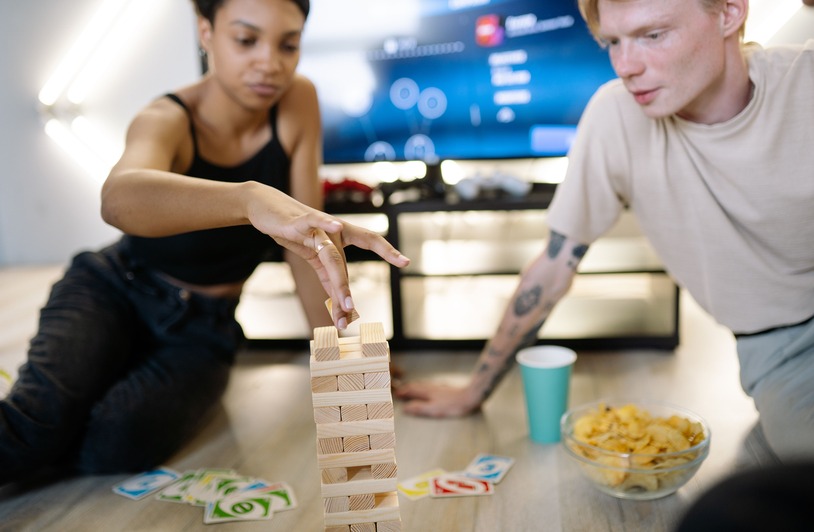 Bring On the Fun and Challenge Friends in GameZone Online Games Two friends enjoying a fun game night with Jenga and cards indoors.