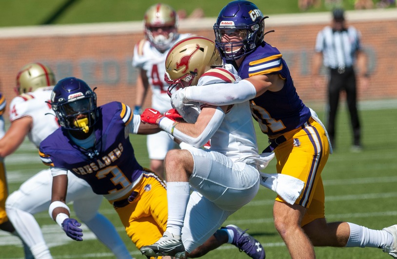 College Football’s Money Shift and the Trust Test for U.S. Fans Two football players in purple and gold uniforms tackle a player in white and red on a sunny outdoor field