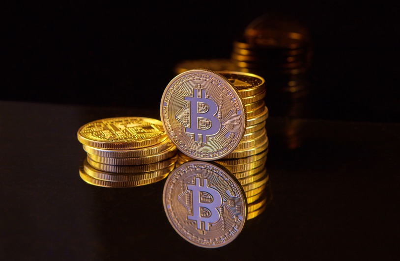Digital Currencies: Shaping the Future of Transactions Two stacks of gold-colored coins with a B symbol on a reflective black surface against a dark background