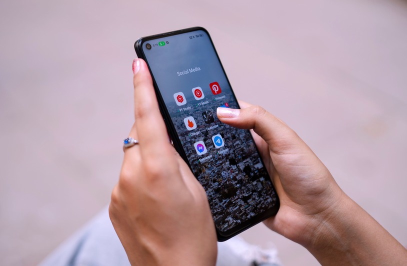 The Apps Winning More Screen Time in 2026 Have One Thing in Common Two hands with pink nails and a ring holding a smartphone displaying a Social Media app folder with colorful icons