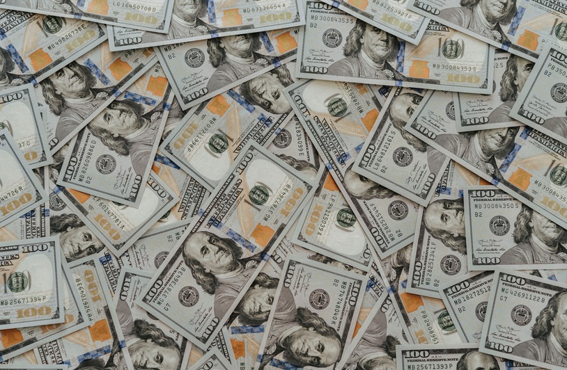 Financial Pressure as a Revenue Engine US hundred dollar bills scattered in abundance creating a financial backdrop.