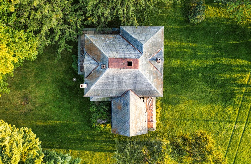 From Your Roof to Your Lawn: How Shifting EPA Rules Are Rewriting the Rules of Home Sustainability A top-down view of an abandoned, derelict cottage surrounded by lush green grass and trees, capturing a peaceful landscape.