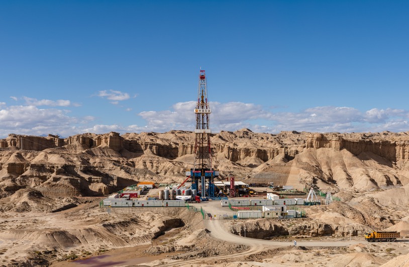 High-Stakes Ecology: How Risk-Intensive Energy Extraction Projects Shape Society’s Future Aerial view of an oil rig amidst desert rock formations, showcasing industrial exploration.