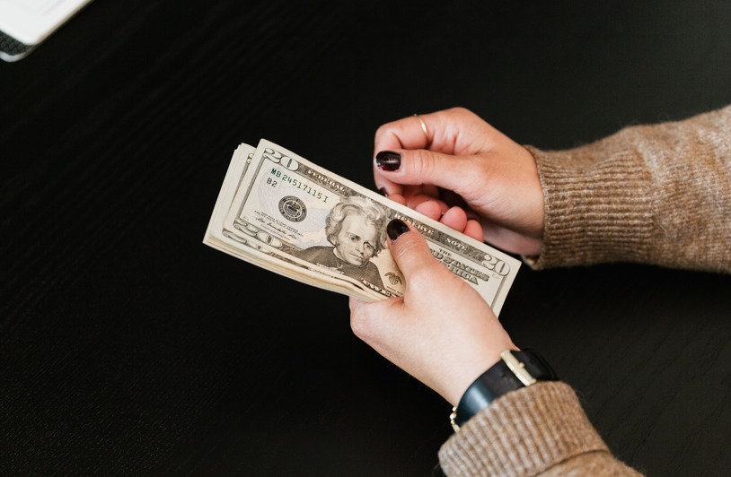 How Americans Really Handle Their Money: Insights into Saving Habits Close-up of hands counting a stack of US dollar banknotes on a dark table.