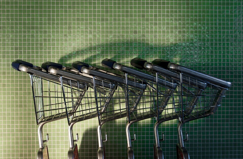 A row of neatly arranged shopping carts in front of a green tiled wall with shadows.