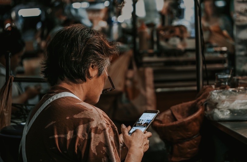 How Social Media Is Reshaping Consumer Trust in Expert Advice A woman with short hair looking down at a smartphone in a busy market environment.