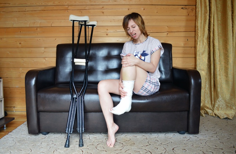 How Soft-Tissue Injuries Create Long-Term Challenges That Many Accident Victims Underestimate Full body of woman with aching leg sitting on couch near pair of crutches
