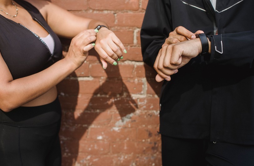 How Wearable Health Trackers Are Transforming Evidence Collection After Accidents Two people in sportswear checking their fitness trackers outdoors against a brick wall.