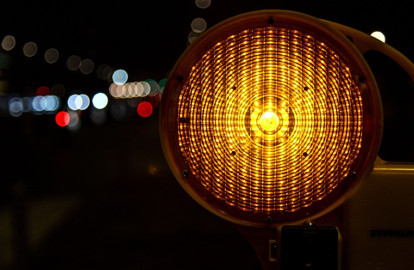 Night Work Zones, Dim Lights, Real Risks: Why Poor Lighting Hurts Riders After Dark A reflective traffic warning light glowing in the nighttime with bokeh effect.