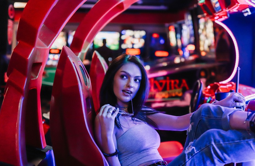 Play Smarter and Unlock VIP Perks with the GameZone Rebate Promo Woman in casual attire enjoying leisure time at a colorful arcade, exuding a relaxed vibe.
