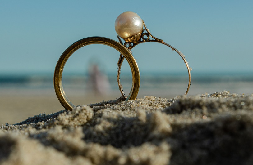 The Art of Combining Pearls and Gold: 14K Gold 9mm Freshwater Pearl Ring Close-up of gold rings on a beach with a blurred ocean background, emphasizing a pearl ring in focus.