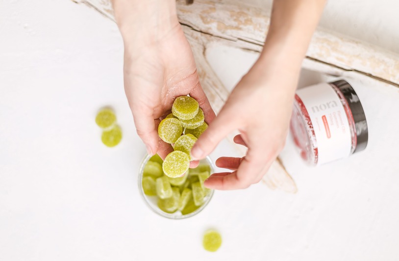 Top-Rated Sleep Gummies: 5 Best Edibles for Relaxation and Restful Close-up of hands holding green CBD gummies above a container, top view.
