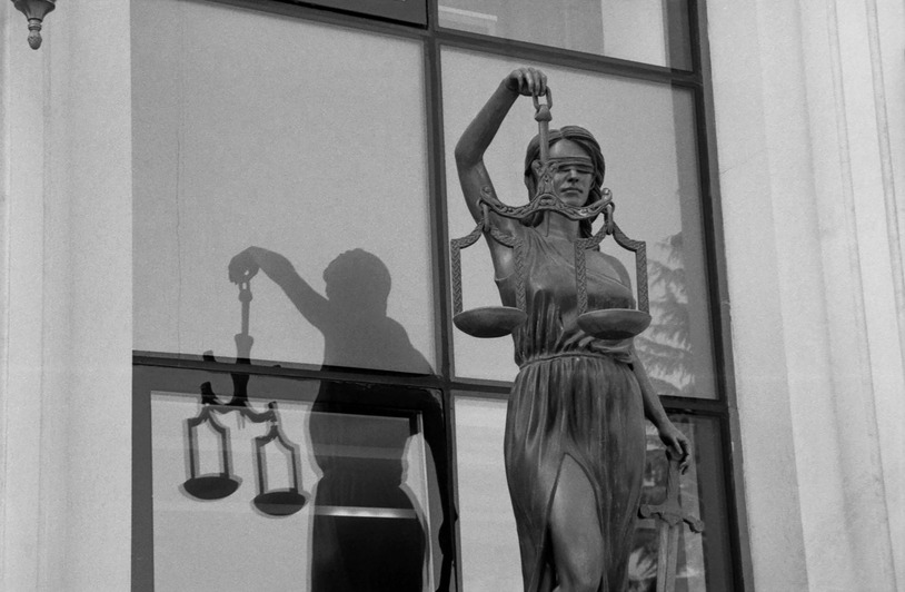 Black and white image of Lady Justice statue reflecting in a window, symbolizing fairness.