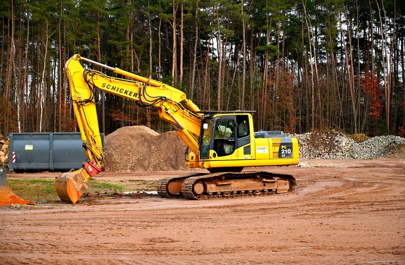 Visibility Challenges When Navigating Around Bulldozers and Cranes A yellow excavator at work in a forested construction site, surrounded by dirt and gravel.