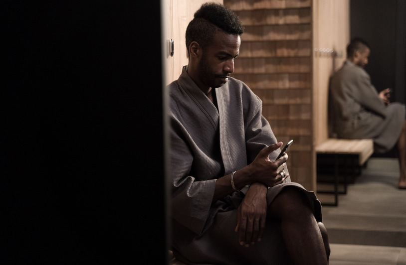 Wellness in 2026: Convenience, Personalization, and Better Access Man in a robe checking phone in a quiet modern dressing room setting.