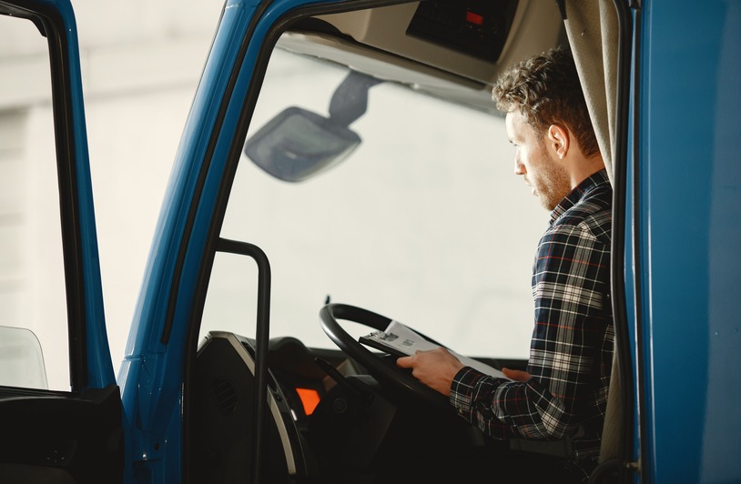 What to Expect During Your FMCSA New Entrant Safety Audit A man sitting in a truck cabin reading a document inside a blue truck, showcasing focused driving preparation.