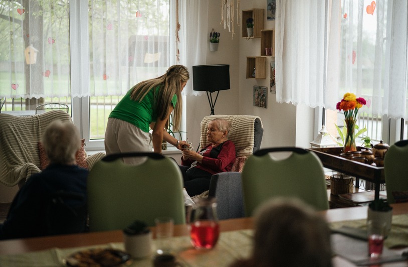 What Myths Cause Families to Miss Real Signs of Nursing Home Neglect? Caregiver assisting elderly women with tea in a cozy nursing home setting.