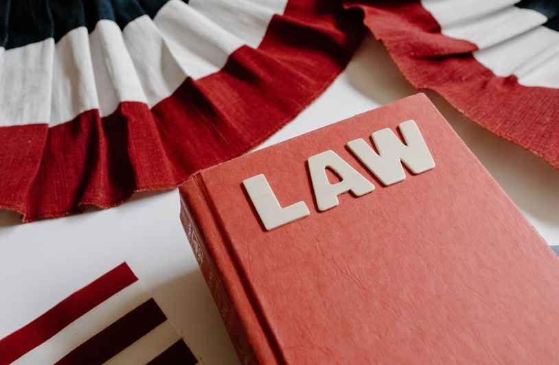 Who Sets the Rules: How Laws Are Formed Long Before Ordinary Citizens Ever See Them A law book with bold letters placed beside a red, white, and black decorative ribbon.