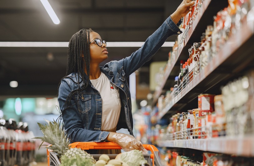African American woman selecting items in a grocery store aisle with a shopping cart.