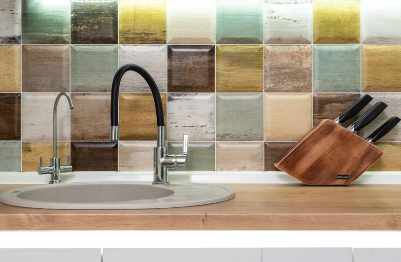 Can You Paint Kitchen Countertops? What Works, and What Does Not Oval gray sink with two faucets on a wood countertop, knife block with black-handled knives, multicolored square tile backsplash