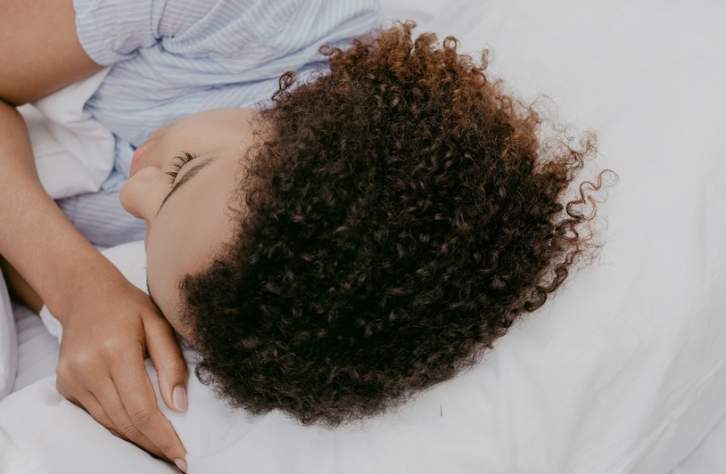 A person sleeping on their side in bed with their head on a pillow