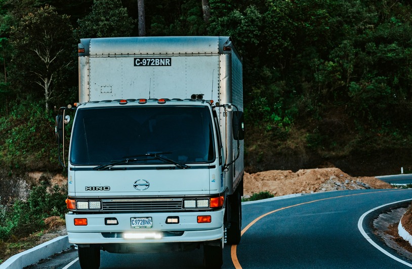 Seven Mistakes That Can Weaken a Texas Delivery Truck Claim White Hino box truck with license plate C-972BNR driving on a curved road bordered by trees and a dirt embankment