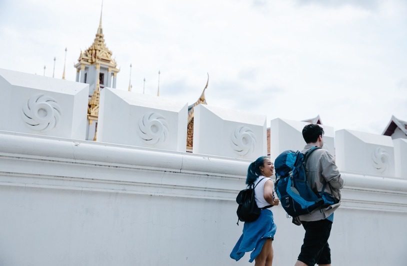 Thailand Solo Travel in 2026 Two backpackers walking alongside a white ornate temple wall with a gold-spired building visible above