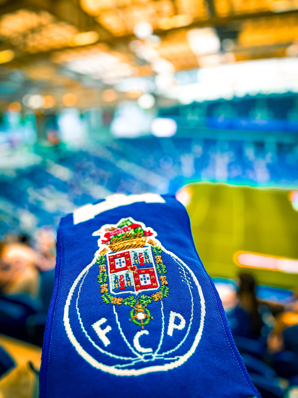 A football scarf held up in a stadium with the stands and pitch in the background.