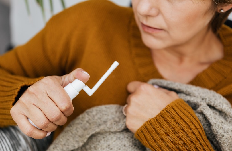 BreathiZen Drops Reviews 2026 (EXPOSED) – Legit Breathing Support Spray Or Overhyped? Adult woman using a mouth spray indoors, wrapped in a sweater