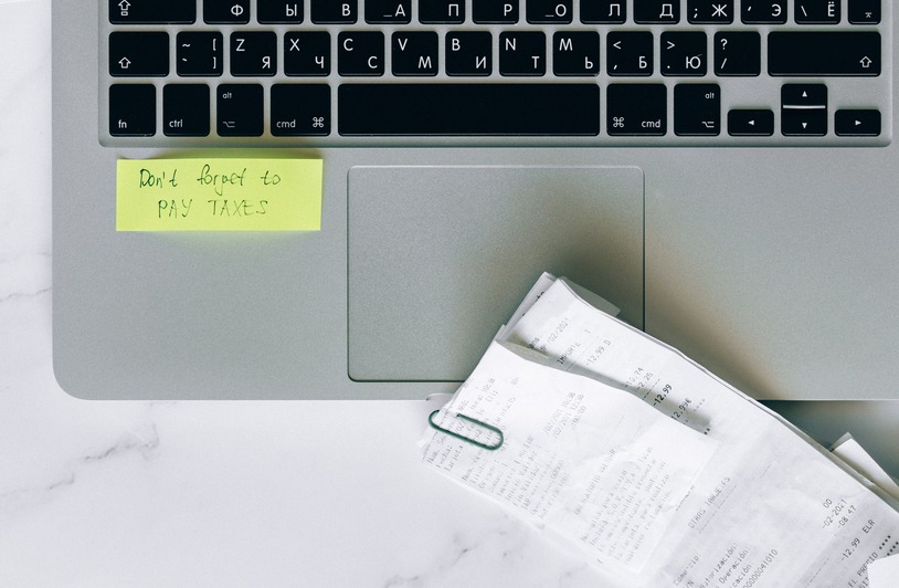 Why Your Property Tax Bill Went Up When Nothing Changed in Your Neighborhood A laptop with a sticky note reminder and receipts, emphasizing tax season organization.