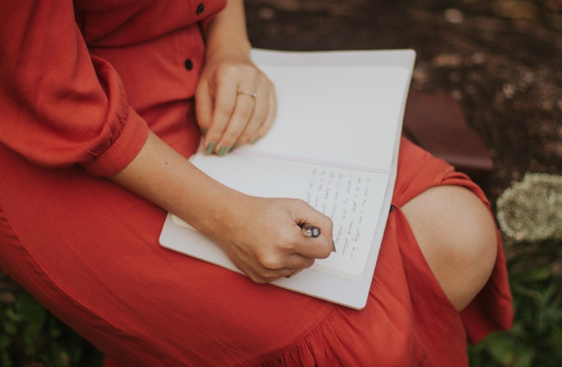 Why Keeping a Recovery Journal Can Help Support Your Seattle Personal Injury Claim A woman in a red dress writing in a journal, outdoors over a leafy background.
