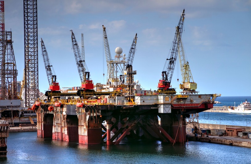 Workers on an offshore oil platform with steel structural framework visible against the sky