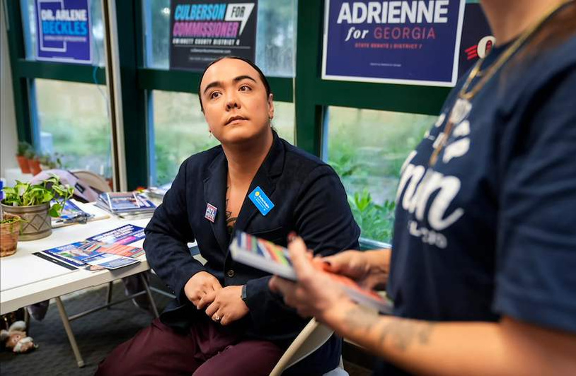 In Georgia, Two Trans Candidates Believe Voters Are Ready for Them Hudgins sits in a chair listening to someone off frame and surrounded by campaign materials.